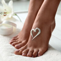 Woman with beautiful feet and cream on white towel, closeup. Spa treatment